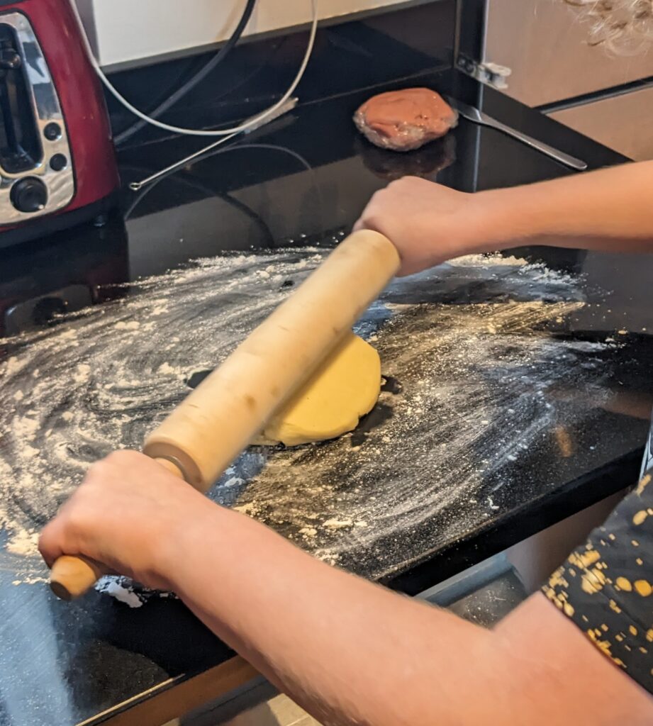 Dough being rolled out with a wooden rolling pin on a slightly floured surface.
